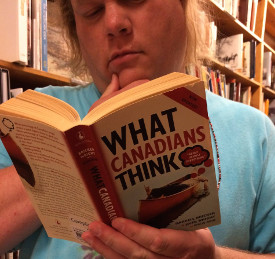 photo of Sean at Powell's City of Books in Portland, Oregon. He appears to be deeply into the book he has in his hands. The book is called What Canadians Think.